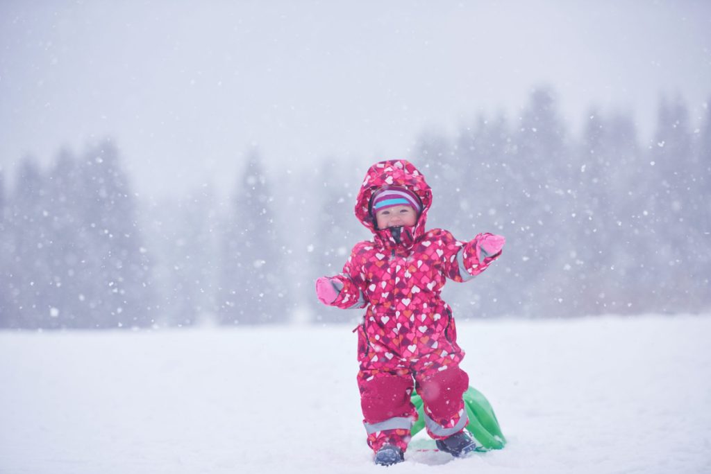 happy family on winter vacation, mom and cute little girl have fun and slide while snow falkes falling